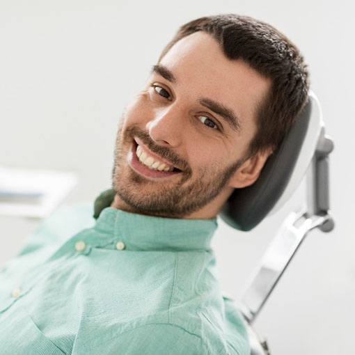 Man in green shirt smiling while relaxing in treatment chair