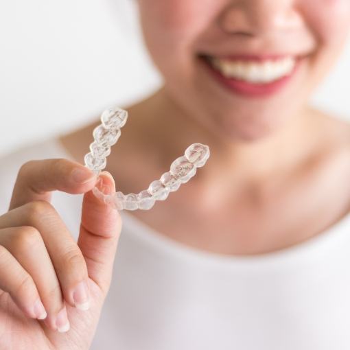 Smiling woman holding Invisalign clear braces tray