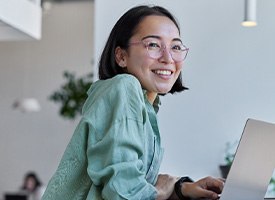 Woman with glasses smiling while working on laptop