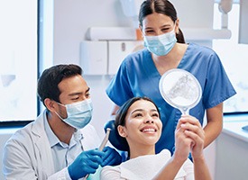 Patient smiling at reflection in handheld mirror with dentist