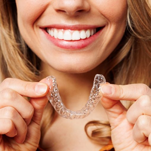 Smiling woman holding clear aligner