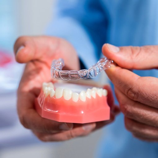 Dentist placing clear aligner on model of teeth