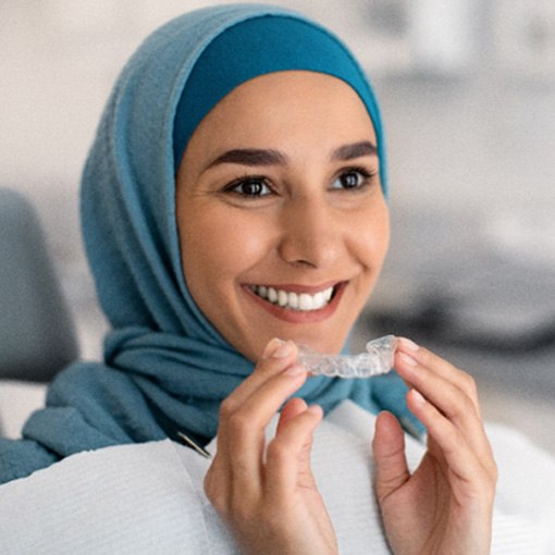 Smiling woman holding clear aligner at dentist's office