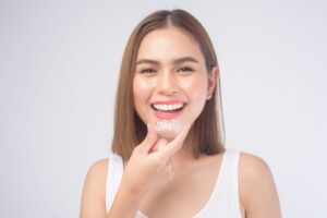 Woman with straight brown hair inserting clear aligner in front of off-white background